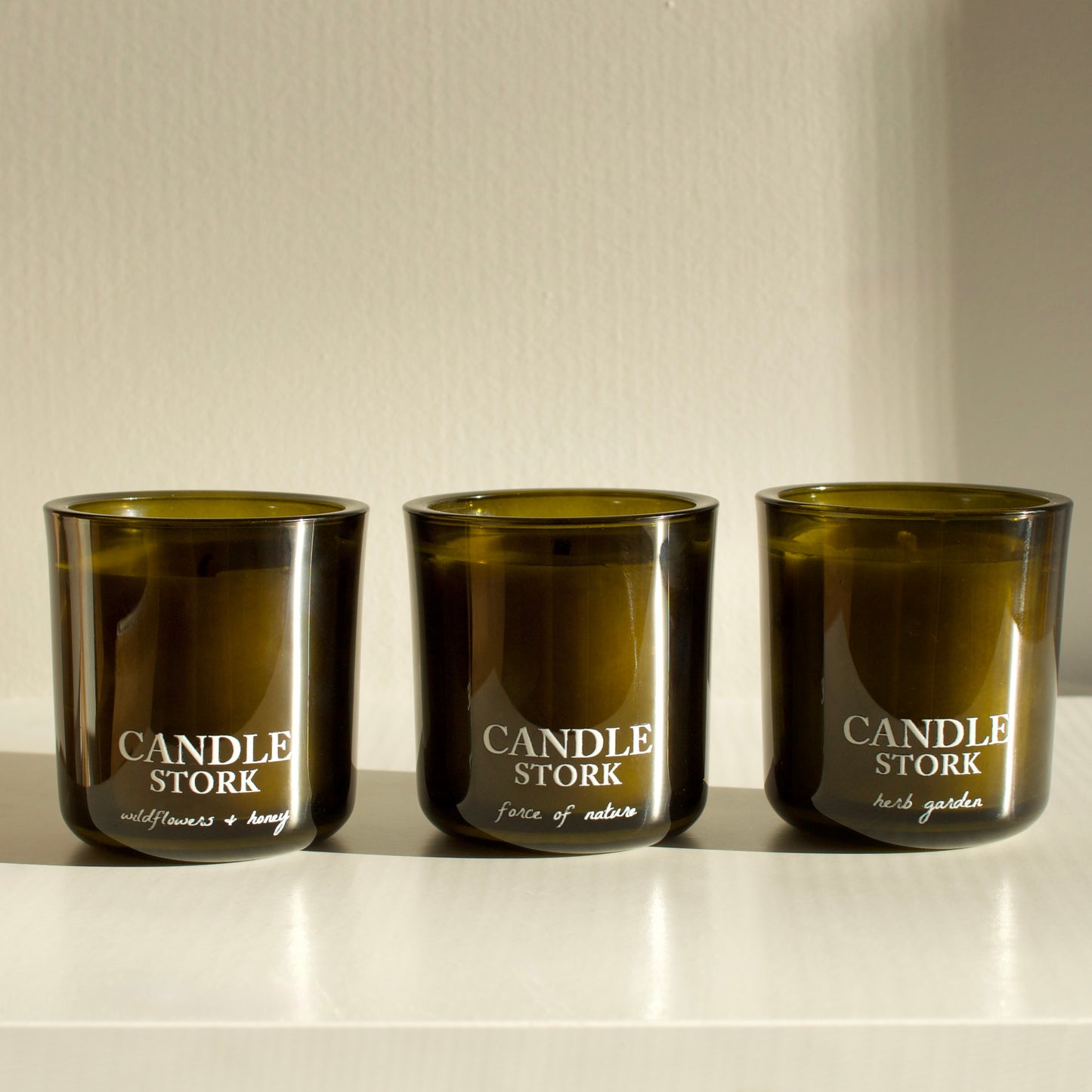 Three green candles labeled 'Candle Stork' on a white surface with a neutral background