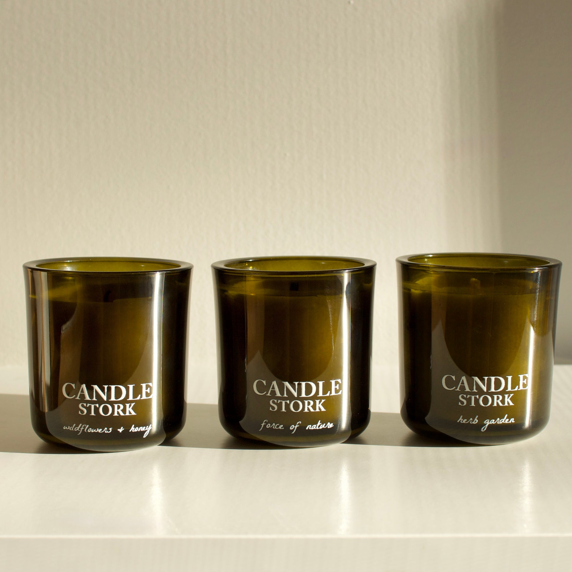 Three green candles labeled 'Candle Stork' on a white surface with a neutral background