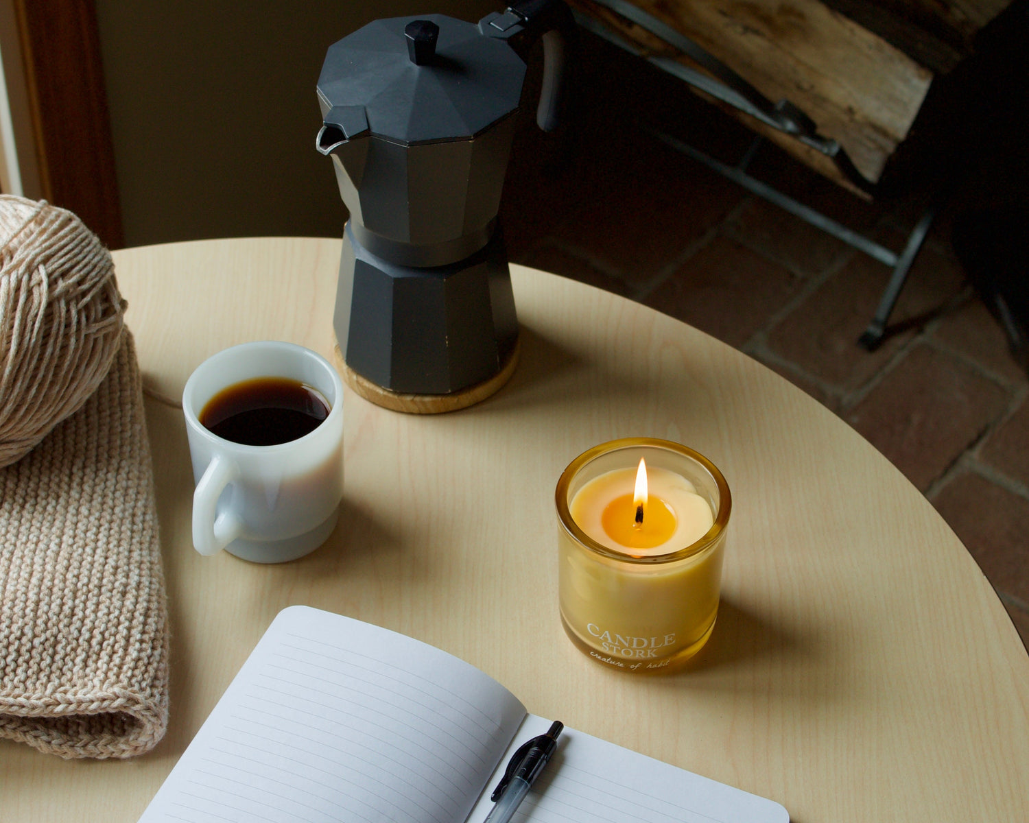 Candle, coffee cup, and open notebook on a wooden table with a warm ambiance.
