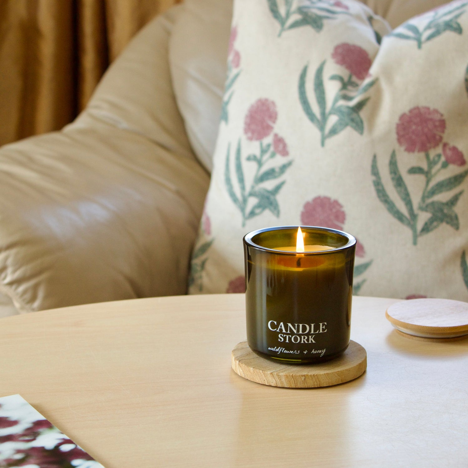 Candle on a coaster on a table with a floral-patterned pillow in the background