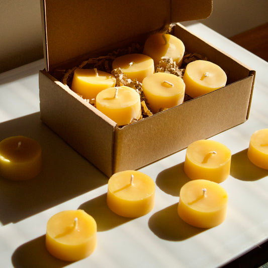 Box of beeswax candles on a light surface with sunlight casting shadows.