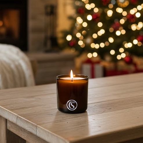 Candle on a wooden table with a Christmas tree and fireplace in the background