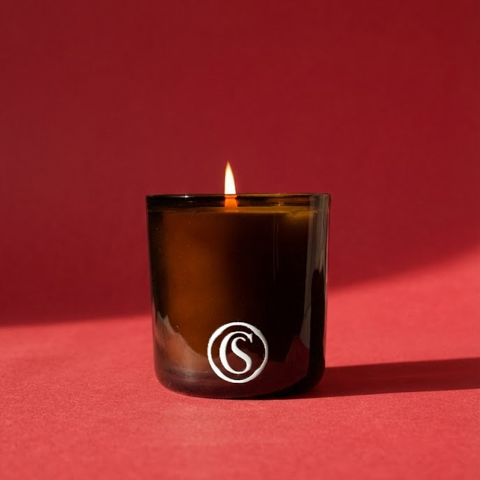 Candle in a brown glass container with a logo on a red background