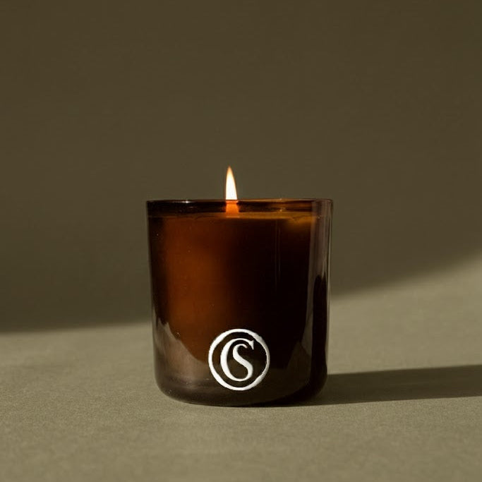 Candle in a amber glass container with a logo on a green background