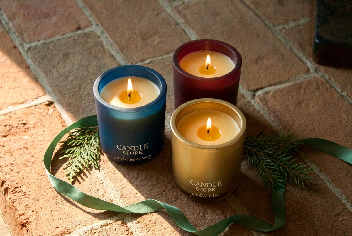 Winter luxe candles on sunlit brick with green ribbon and greenery